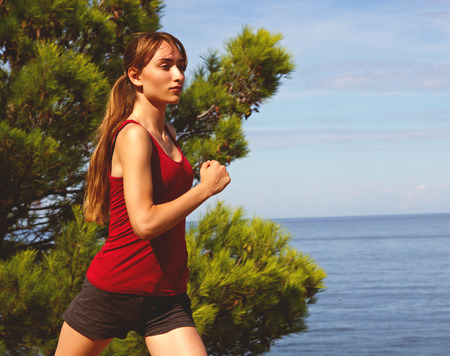 Runner jogging in sunny bright light summer sea. Female fitness model training. Female runner jogging during outdoor workout on beach.の写真素材