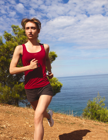 Runner jogging in sunny bright light summer sea. Female fitness model training. Female runner jogging during outdoor workout on beach.の写真素材