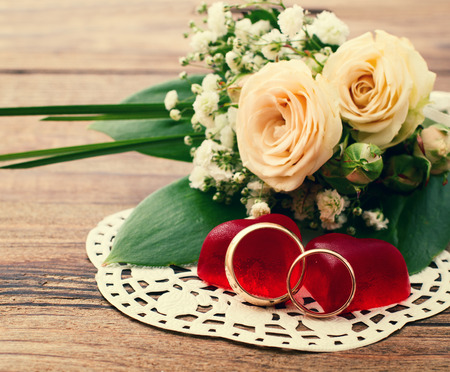 Bridal bouquet of white flowers on wooden surface. Wedding flowers of delicate roses wedding rings. Wedding bouquet background. Empty wooden tabletopの写真素材