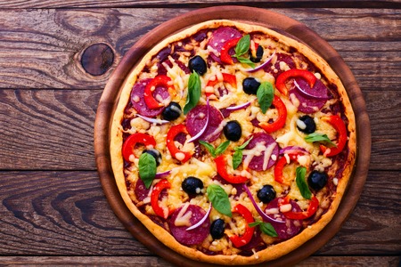 Pizza with ham peppers and olives with delicious fresh food on a wooden table. Ingredients tomatoes, salami and spices for pizza.の写真素材