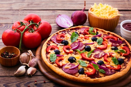 Pizza with ham peppers and olives with delicious fresh food on a wooden table. Ingredients tomatoes, salami and spices for pizza.の写真素材