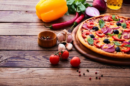 Pizza with ham peppers and olives with delicious fresh food on a wooden table. Ingredients tomatoes, salami and spices for pizza.の写真素材