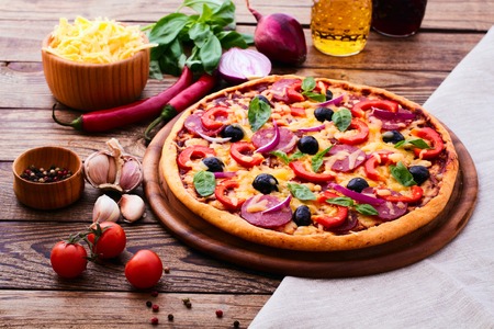 Pizza with ham peppers and olives with delicious fresh food on a wooden table. Ingredients tomatoes, salami and spices for pizza.の写真素材