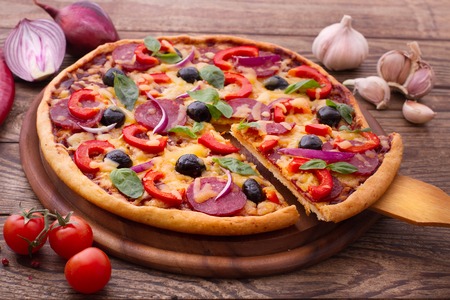 Pizza with ham peppers and olives with delicious fresh food on a wooden table. Ingredients tomatoes, salami and spices for pizza.の写真素材