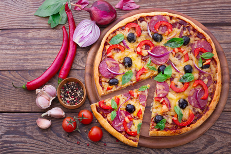 Pizza with ham peppers and olives with delicious fresh food on a wooden table. Ingredients tomatoes, salami and spices for pizza.の写真素材