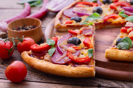 Pizza with ham peppers and olives with delicious fresh food on a wooden table. Ingredients tomatoes, salami and spices for pizza.の写真素材