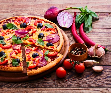 Pizza with ham peppers and olives with delicious fresh food on a wooden table. Ingredients tomatoes, salami and spices for pizza.の写真素材