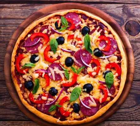 Pizza with ham peppers and olives with delicious fresh food on a wooden table. Ingredients tomatoes, salami and spices for pizza.の写真素材