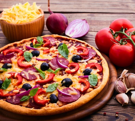 Pizza with ham peppers and olives with delicious fresh food on a wooden table. Ingredients tomatoes, salami and spices for pizza.の写真素材