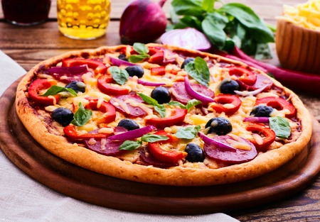 Pizza with ham peppers and olives with delicious fresh food on a wooden table. Ingredients tomatoes, salami and spices for pizza.の写真素材