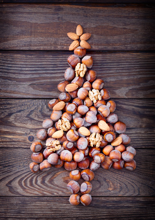 Christmas tree made of hazelnuts with red baubles and gifts on wooden backgroundの写真素材