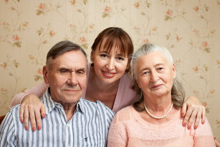 Happy family. Portrait of elderly couple and adult daughter happily looking at camera. Senior man, woman with their caregiver at home.の写真素材