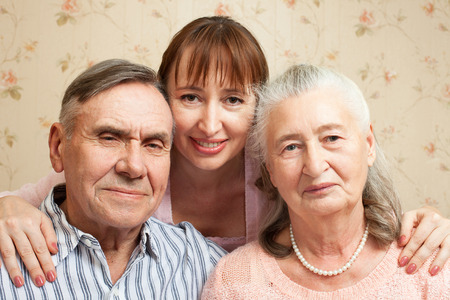 Happy family. Portrait of elderly couple and adult daughter happily looking at camera. Senior man, woman with their caregiver at home.の写真素材