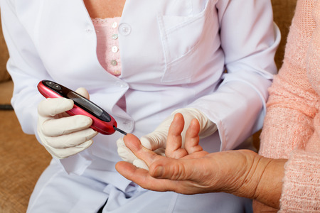 Nurse takes test for sugar in blood of elderly woman at home. Seniors woman with her caregiver at homeの写真素材