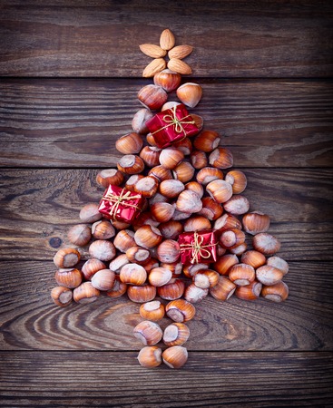 Christmas tree made of hazelnuts with red baubles and gifts on wooden backgroundの写真素材