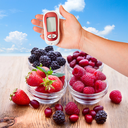 Woman testing for high blood sugar. Bowls overflowing with summer berriesの写真素材