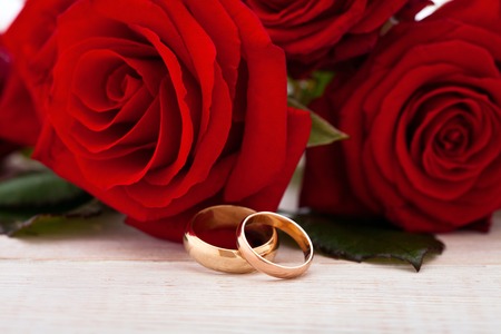 Wedding rings and wedding bouquet of red roses on wooden table. horizontallyの写真素材