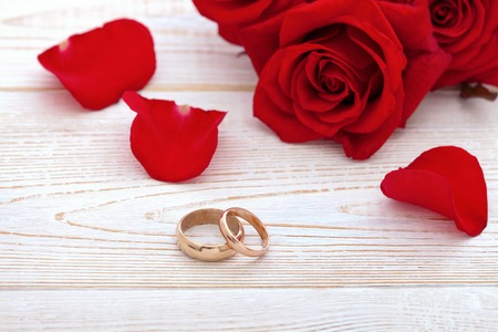 Wedding rings and wedding bouquet of red roses on wooden table. horizontallyの写真素材