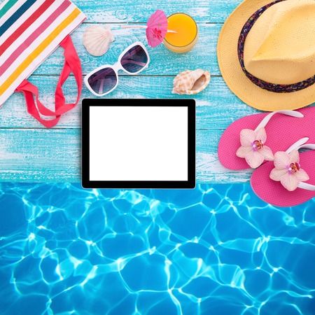 Blank empty tablet computer on beach. Trendy summer accessories on wooden background pool. Sunglasses, orange juice and flip-flops on beach. Tropical flower orchid. Flat mock up for design.の写真素材