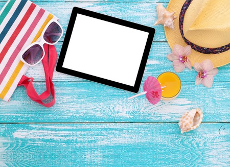Blank empty tablet computer on beach. Trendy summer accessories on wooden background pool. Sunglasses, orange juice and flip-flops on beach. Tropical flower orchid. Flat mock up for design.の写真素材