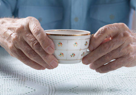 An elderly man drinks tea at home. Senior man holding cup of tea in their hands at table close-up