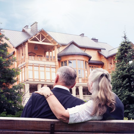 Elderly couple sitting on bench in garden near house. Concept of investing money in real estate, property insurance.の写真素材