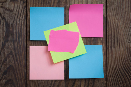 Multicolored paper stickers note on wooden background. Blank forms for workers notes