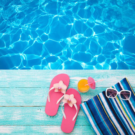 Summer Holidays in Beach Seashore. Summer drinks. Summer rest. Fashion accessories summer flip flops, hat, sunglasses on bright turquoise board near the pool Summer Holidays in Beach Seashore. Summer drinks. Summer rest. Fashion accessories summer flip flops, hat, sunglasses on bright turquoise board near the pool