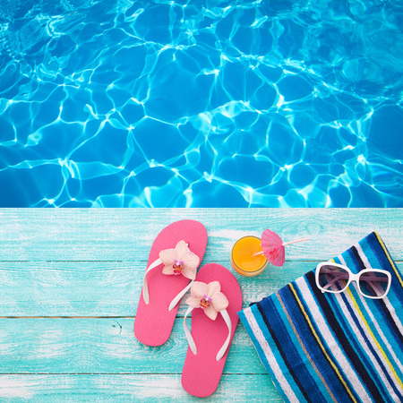 Summer Holidays in Beach Seashore. Summer drinks. Summer rest. Fashion accessories summer flip flops, hat, sunglasses on bright turquoise board near the pool