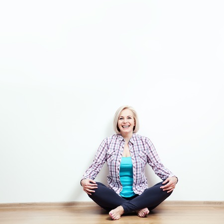 Happy woman sitting on the floor with crossed legs in fashionable clothing on white background in studioの写真素材