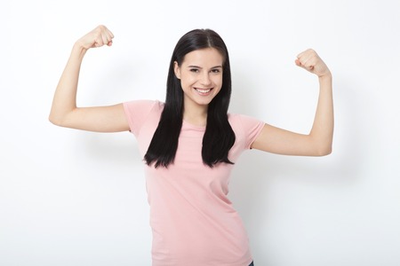 Strong woman. Beautiful young woman showing her muscularity and looking at camera while isolated on whiteの写真素材