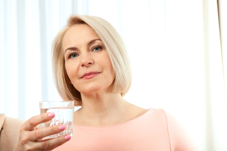 Portrait beautiful middle aged woman drinking water in the morning. Woman's face close upの写真素材