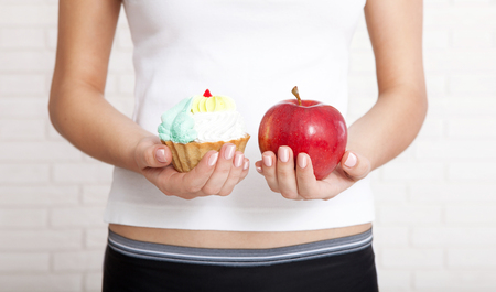 Woman chooses to eat an apple or cake. Woman holding an apple and a cake close up.の写真素材