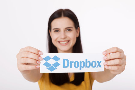 KIEV, UKRAINE - August 22, 2016: Woman hands holding Dropbox logotype sign printed on paper on white...
