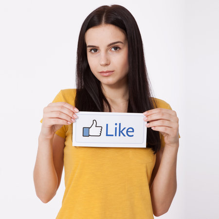 KIEV, UKRAINE - August 22, 2016: Woman hands holding facebook thumbs up sign printed on paper on white background. Facebook is well-known social networking service.のeditorial素材