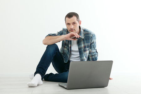 Young handsome man relaxing on floor and using laptop, smart phone at home.の写真素材