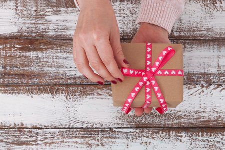 Woman holding presents gift box laid on wooden table background