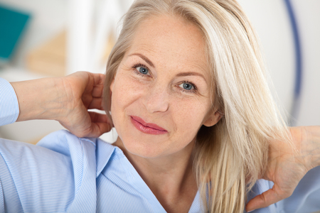 Modern businesswoman. Beautiful middle aged woman looking at camera with smile while siting in the office.の写真素材