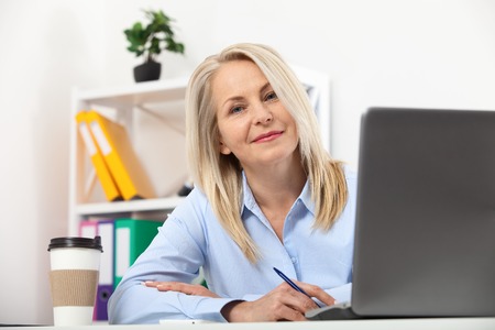 Business woman working in office with documents. Beautiful middle aged woman looking at camera with smile while siting in the office.の写真素材