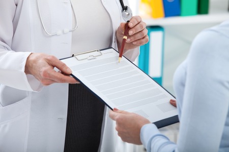 Female doctor holding application form while consulting patient at hospitalの写真素材