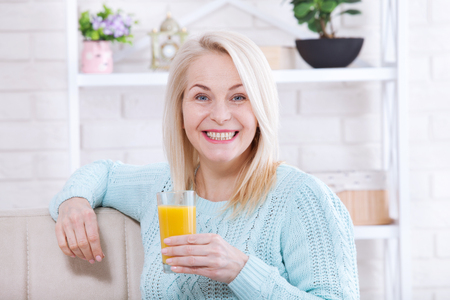 Woman drinking orange juice smiling. Beautiful middle aged Caucasian model face closeup.の写真素材