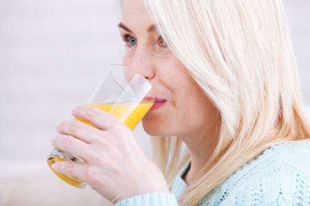 Woman drinking orange juice smiling. Beautiful middle aged Caucasian model face closeup.の写真素材