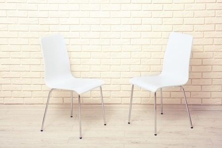 White chairs near the white wall for interior or graphic backgrounds. The chairs can be used to represent interview sessions or waiting rooms for ads purpose.の写真素材