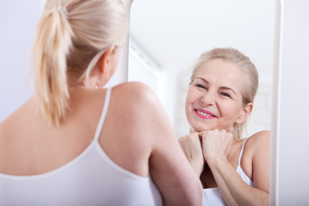 Forty years old woman looking at wrinkles in mirror. Plastic surgery and collagen injections. Makeup. Macro face. Selective focusの写真素材