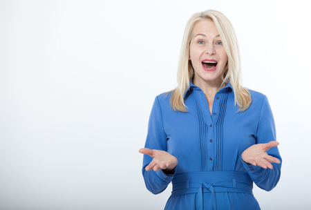 Portrait of happy middle aged woman. Surprised happy woman looking with her mouth open and holding her arms out in excitement. Isolated over white backgroundの写真素材