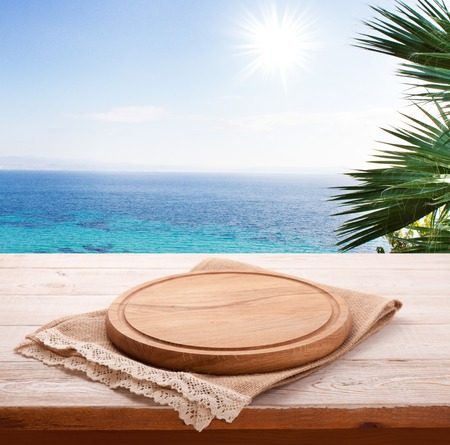 Pizza board, with tablecloth on wooden table and summer sea background.の写真素材