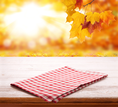 Empty wooden deck table with tablecloth over bokeh autumn leaves background. Kitchen background, product montage display. Mock up .の写真素材