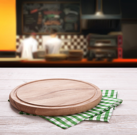 Empty pizza board with tablecloth on the table and pizzeria blurred backgroundの写真素材
