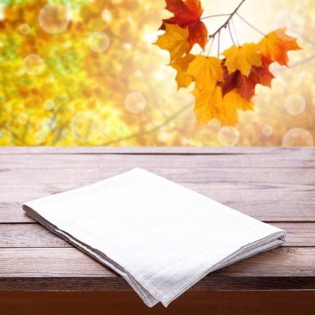 Empty wooden deck table with tablecloth over bokeh autumn leaves background. Kitchen background, product montage display. Mock up .の写真素材