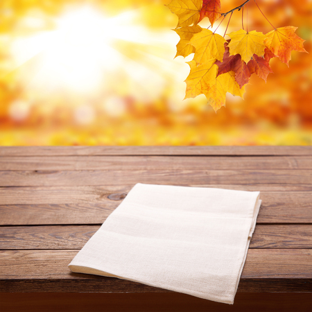 Empty wooden deck table with tablecloth over bokeh autumn leaves background.の写真素材